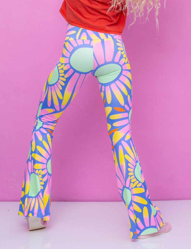 A woman wearing colourful flower pattern high wasted flares standing in front of a pink wall