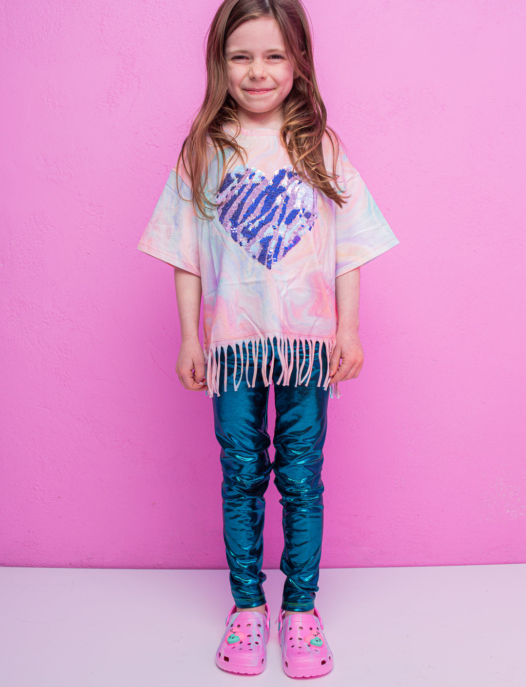 A child wearing blue shiny leggings and a pink t-shirt with a purple heart