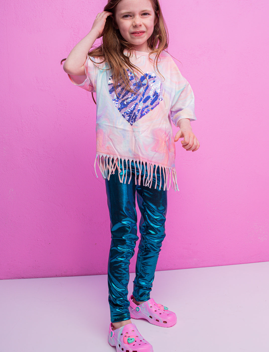 A child wearing blue shiny leggings and a pink t-shirt with a purple heart with one arm up