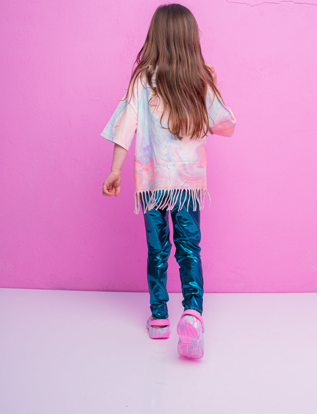 A child walking away wearing blue shiny leggings and a multi coloured t-shirt