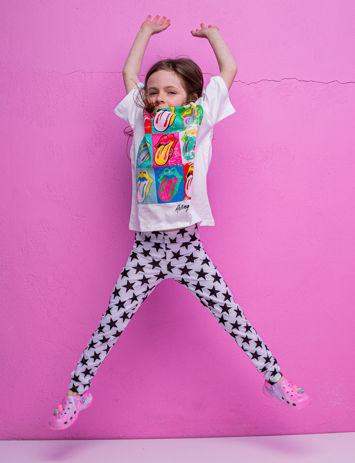 A child jumping in the air with their arms up wearing white leggings with black stars  and a colourful t-shirt