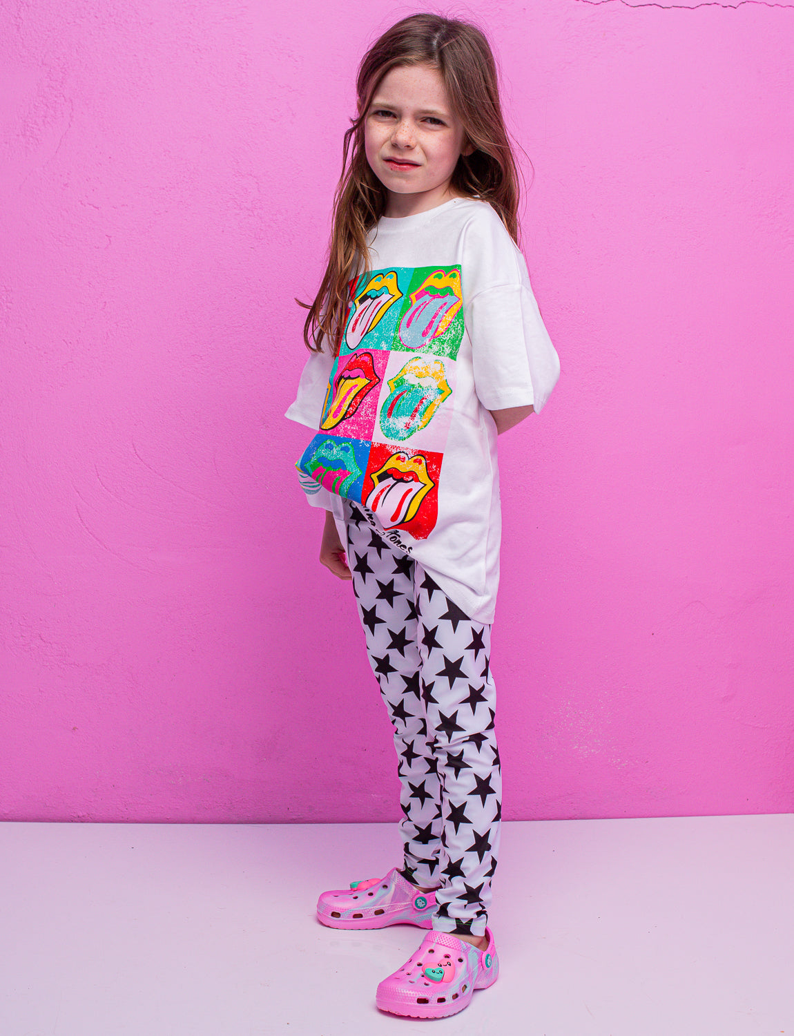 A child wearing white leggings with black stars and a colourful t-shirt and pink crocs