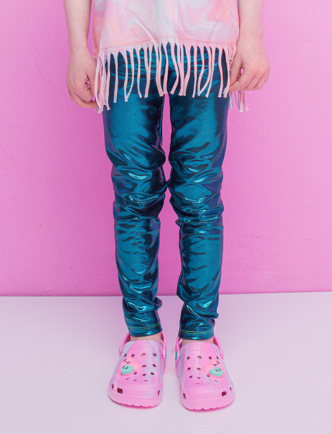 A child wearing blue shiny leggings and pink crocs