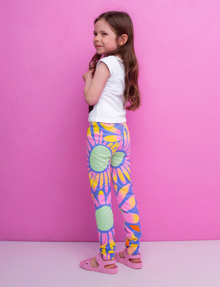 Young girl wearing colorful tie-dye leggings against a pink background