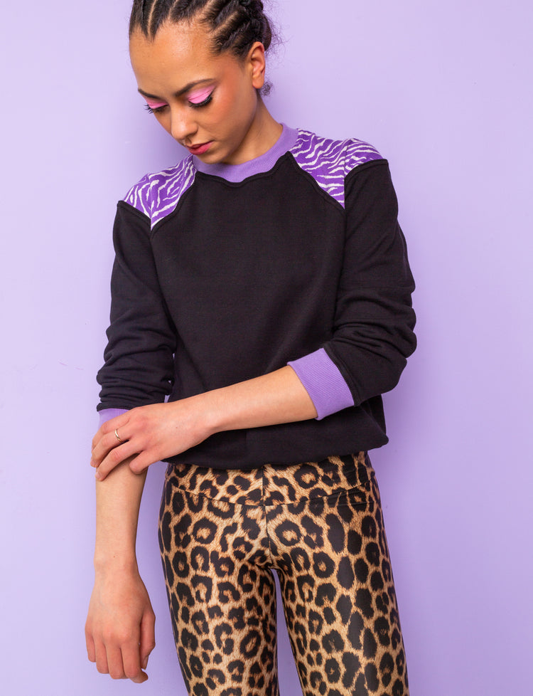 woman wearing a black sweatshirt with purple zebra print shoulders and leopard print leggings