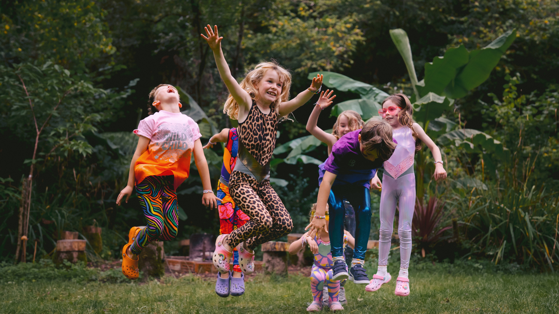 Children in colorful outfits jumping in a garden