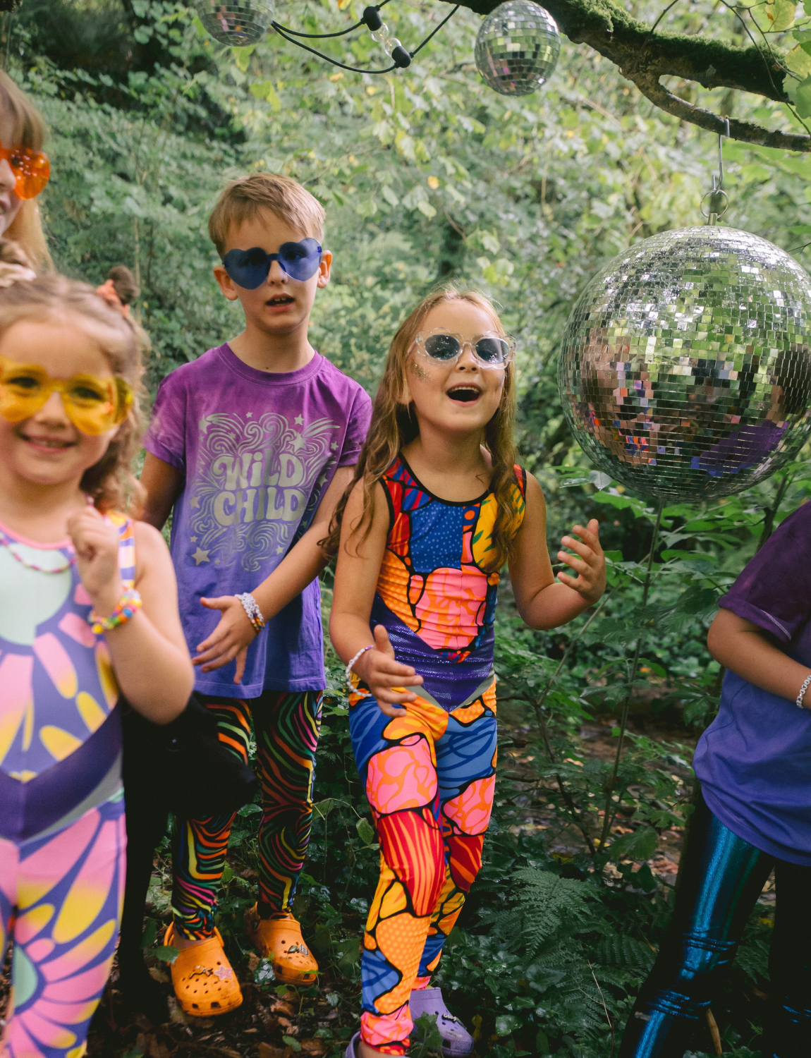 Children in colorful outfits with disco balls in a forest setting