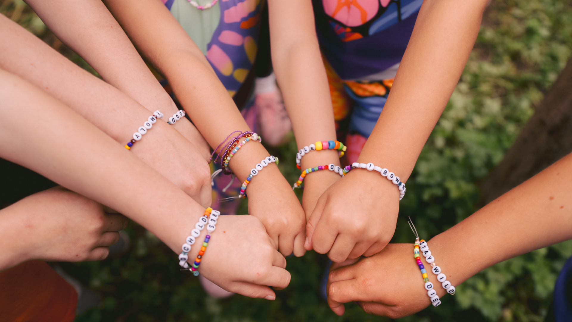 Children's hands with colorful bracelets held together against a natural background